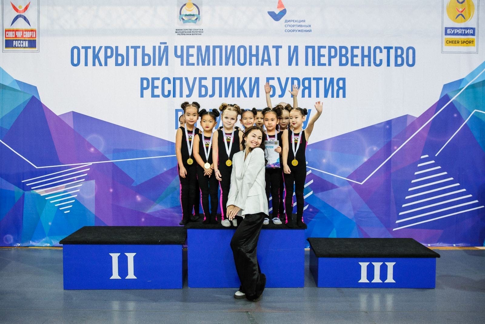 Юные спортсменки с медалями и тренером на пьедестале соревнований в Бурятии